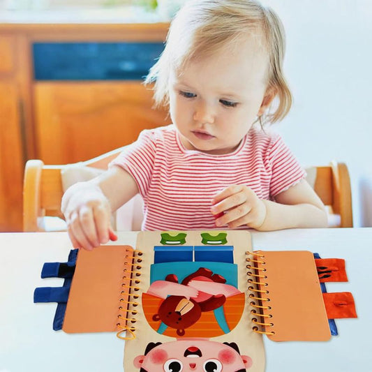Jeune enfant d'environ 18 mois manipulant seul le livre sensoriel en bois Montessori à table